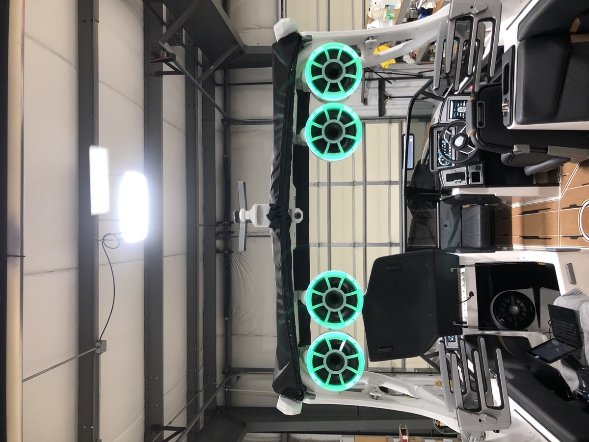 Wake boat tower with four teal-lit tower speakers in the shop