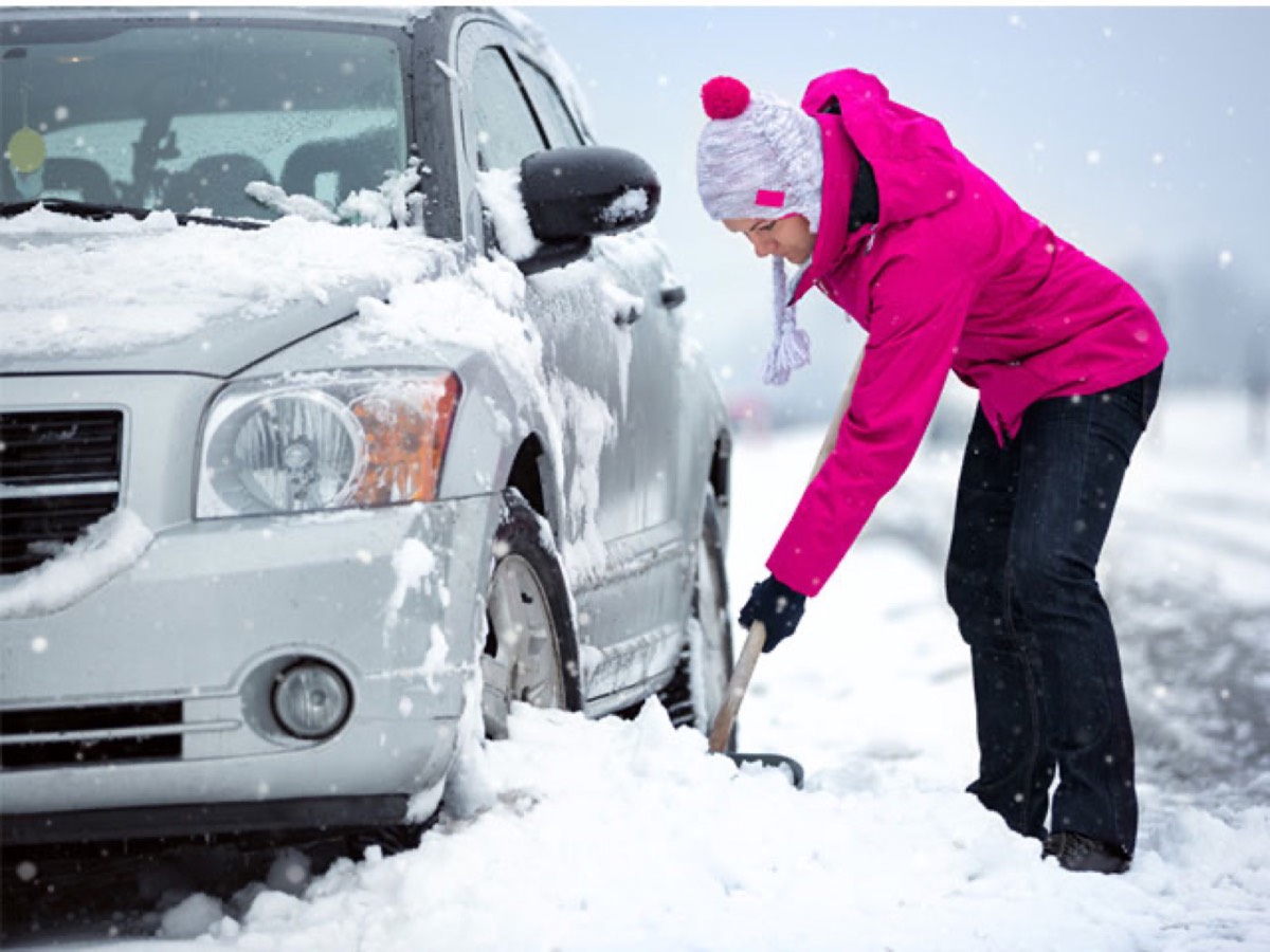 Driver scraping snow off a car in winter